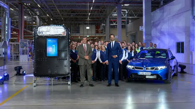 แบตเตอรี่แรงดันสูงที่มีป้าย #1 ตั้งแสดงข้างผู้บริหาร พนักงาน และรถยนต์ BMW ในพิธีเปิดโรงงาน Irlbach-Straßkirchen
