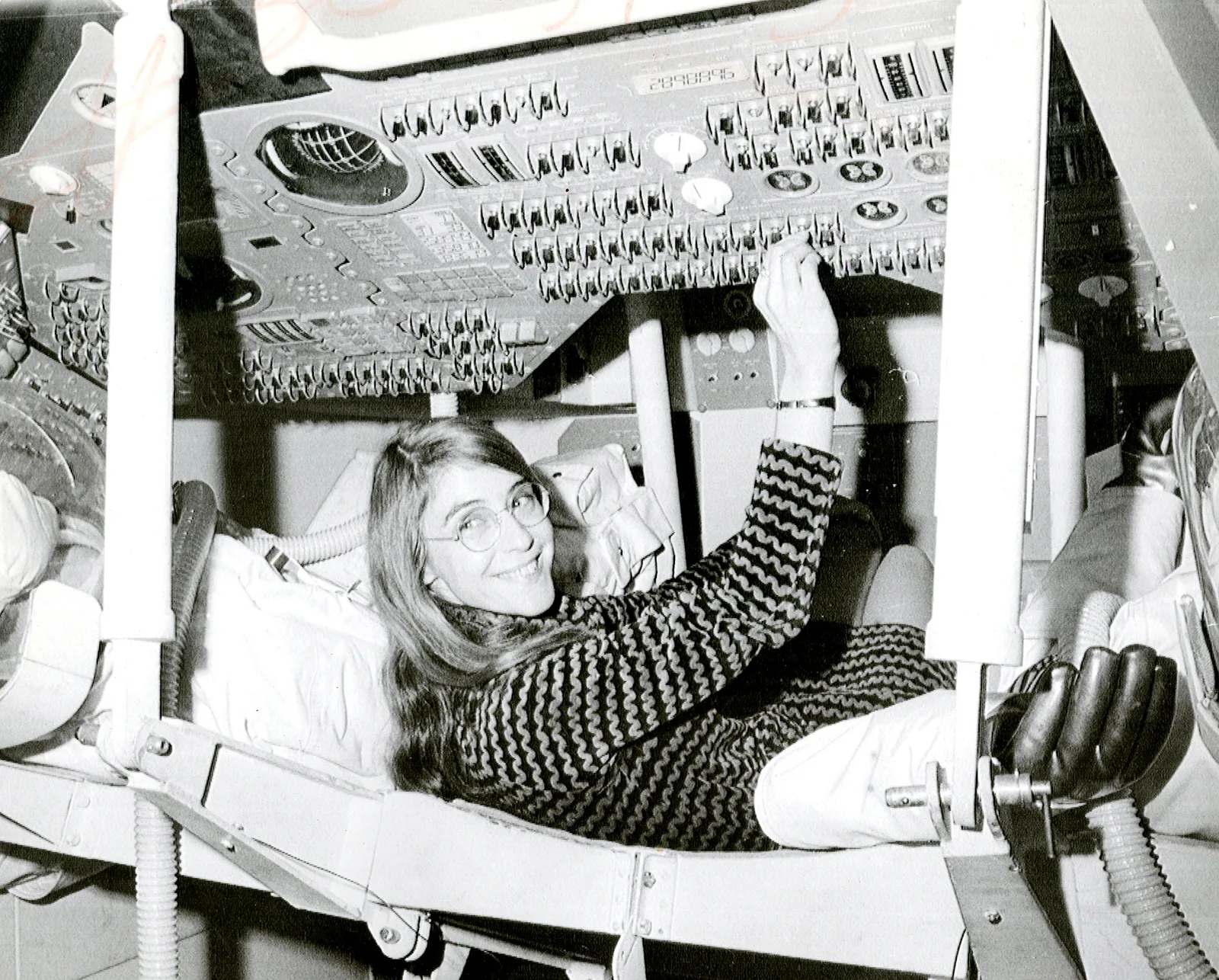 Margaret Hamilton นอนในแบบจำลองยานบังคับการ Apollo และเอื้อมมือกดสวิตช์บนแผงควบคุม